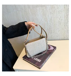 Detail of woven texture handbag with khaki leather strap and silver chain on a book