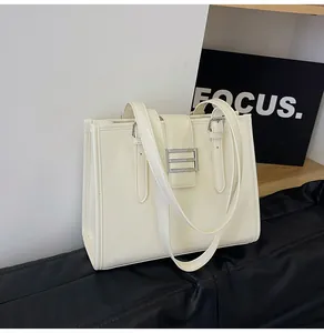 Detail of creamy white tote bag with silver metal buckles and textured leather finish