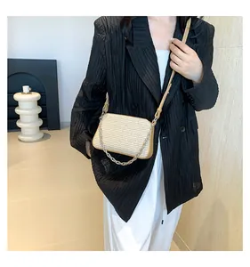 Detail of cream woven shoulder bag with brown trim and metallic chain strap on a model