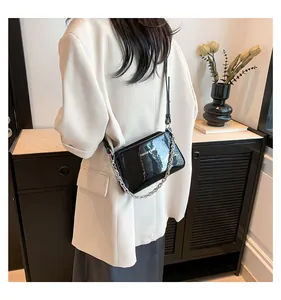 Detail of glossy patent leather texture and chunky silver chain on the black shoulder bag