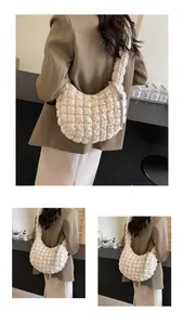 Detail of a quilted puffy crescent bag in off-white fabric with a metal tassel charm