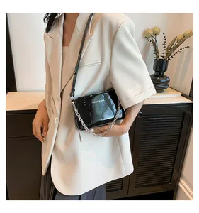 Close-up of black glossy patent leather shoulder bag with silver chain and white logo