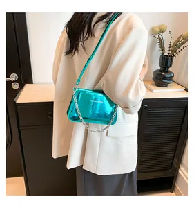 Detailed view of glossy metallic cyan crossbody bag with silver chain strap on model
