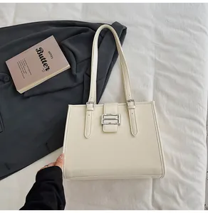 Detail of cream tote bag with silver buckle on a textured fabric and blazer background