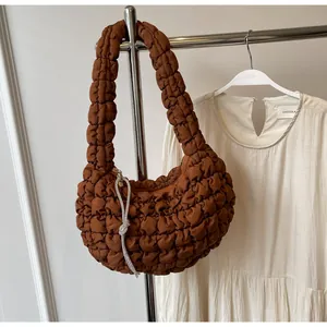 Detail view of brown quilted cloud bag with rhinestone knot charm on a garment hanger