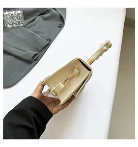 Détail du sac en cuir verni crème montrant la boucle dorée et la poignée torsadée unique