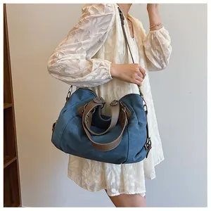 Grand sac cabas en toile bleue porté par un mannequin avec anses en cuir brun et rivets
