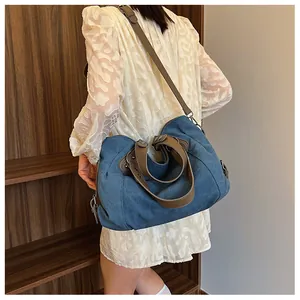 Détail du sac cabas en toile bleue avec anses en cuir marron et bandoulière réglable