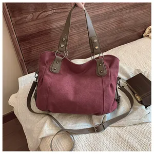 Détail du cabas en toile bordeaux avec anses marron et rivets métalliques sur un lit