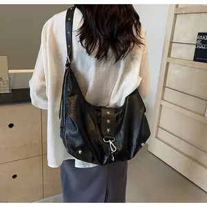 Detail of black faux leather crescent tote bag featuring silver star rivets and metal buckle