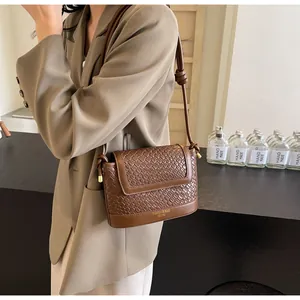 Sac bandoulière marron avec texture tressée porté sur un blazer beige élégant