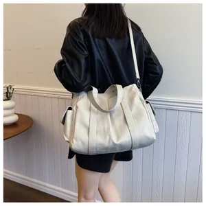 Modell trägt eine große cremefarbene Tote-Bag aus Kunstleder mit praktischen Seitentaschen