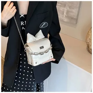 Detail van de crème mini crossbodytas met grote strik en zilveren kettingriem