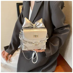 Detailopname van zilveren metallic tas met grote strik en vierkante draaisluiting gesp