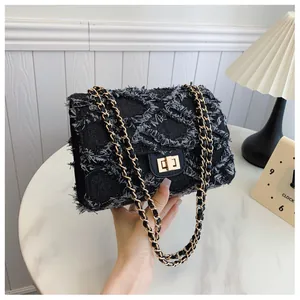 Détail d'un sac bandoulière en denim noir avec matelassage effiloché et fermoir doré