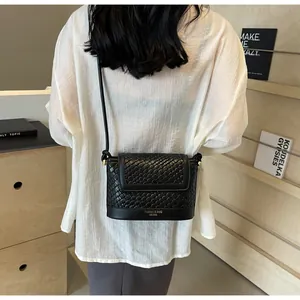 Détail d'un sac à bandoulière noir tressé avec logo doré porté par un mannequin de dos