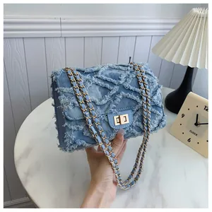 Détail d'un sac à bandoulière en denim bleu avec matelassage, bords effilochés et chaîne dorée