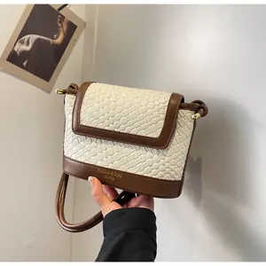 Détail d'un sac bandoulière tissé crème avec bordure marron et lettrage doré élégant