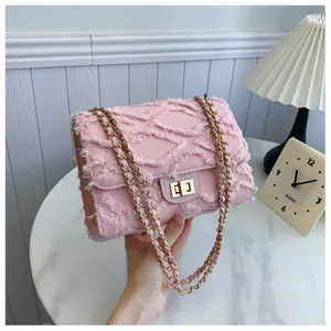 Détail de la texture denim effilochée rose et chaîne dorée du sac à rabat femme
