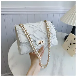 Détail du sac en denim matelassé blanc cassé avec bords effilochés et chaîne dorée
