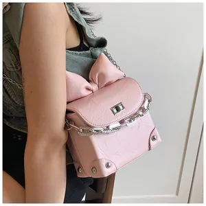 Detailweergave van de roze tas met strik, getextureerd leer en metalen kettingriem