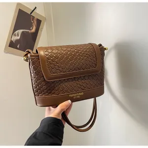 Gros plan sur la texture tressée marron et le marquage doré d'un sac bandoulière chic