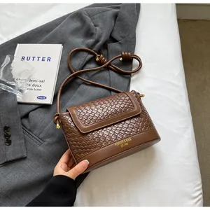 Détail du sac bandoulière marron tressé avec logo doré et bandoulière à nœuds élégante