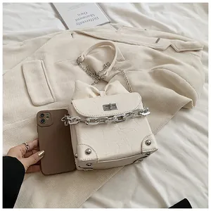Detailopname van de crèmekleurige tas met strik en zilveren ketting op een beige jas