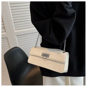 Detail of cream croc-effect crossbody bag with silver twist lock and chain strap on a model
