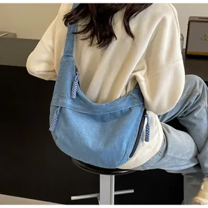 Détail latéral du sac demi-lune en denim bleu avec des breloques boules tressées
