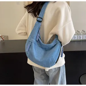 Vue détaillée du sac besace en denim bleu clair avec bandoulière noire et tirette violette