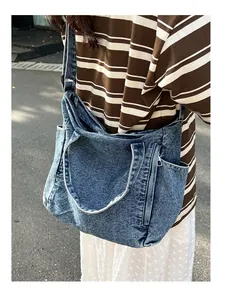 Outdoor model shot of a blue washed denim messenger bag with adjustable shoulder strap