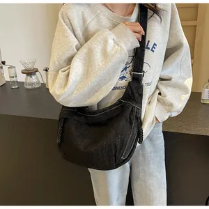 Détail d'un sac bandoulière en denim noir avec surpiqûres blanches et tirette tressée