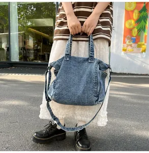 Outdoor shot showing a washed blue denim messenger bag with dual handles and crossbody strap