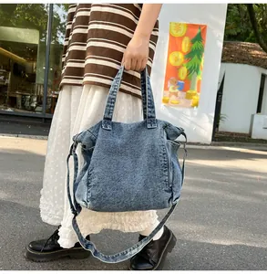 Detailed view of washed blue denim messenger bag with handles and long strap in outdoor setting