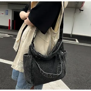 Detailed view of black washed denim messenger bag featuring wide straps and side pockets