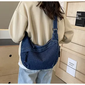 Sac bandoulière en denim bleu avec surpiqûres blanches et tirette de fermeture tressée