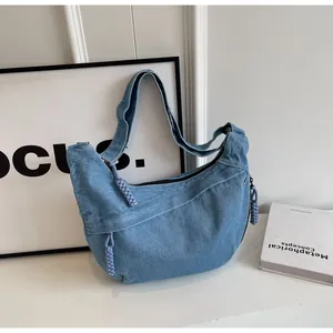 Détail du sac hobo en denim bleu clair avec pendentifs tressés violets et zip argenté