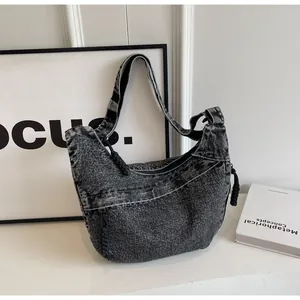 Détail du sac croissant en jean noir avec nœud de fermeture tissé et texture lavée