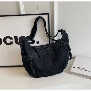 Détail du sac croissant en denim noir avec coutures blanches contrastées et nœud tissé