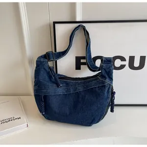 Détail du sac croissant en denim bleu foncé avec surpiqûres blanches et pompon tissé