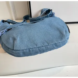 Gros plan du sac hobo en jean bleu clair montrant la texture et le zip tissé violet