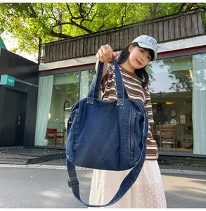 Detail view of large navy blue denim messenger bag with adjustable strap in street style