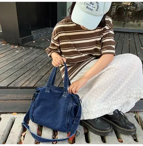 Detail view of large dark blue denim messenger bag worn by a model in casual street style