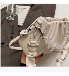 Detail van crème plissé schoudertas met zilveren hardware en kralen decoratie
