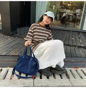 Detail of a large denim messenger bag styled with a casual striped shirt and white skirt
