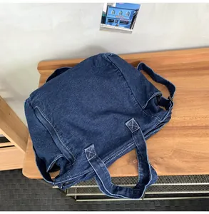 Detail of dark blue denim messenger bag showing reinforced stitching and wide shoulder strap