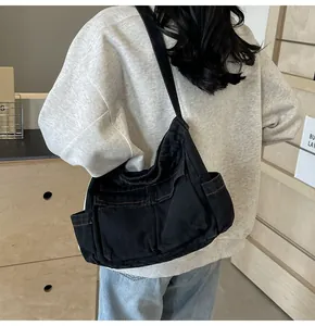 Detail of black denim crossbody bag featuring orange contrast stitching and large pockets