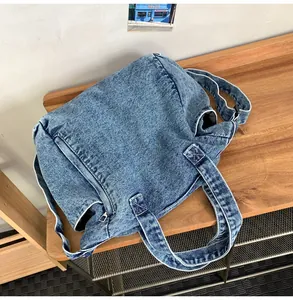 Detail of blue denim messenger bag showing texture, zippers, and side pocket on wood