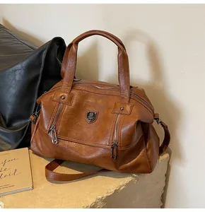 Detail of vintage brown leather tote bag showing zippers and metallic shield emblem